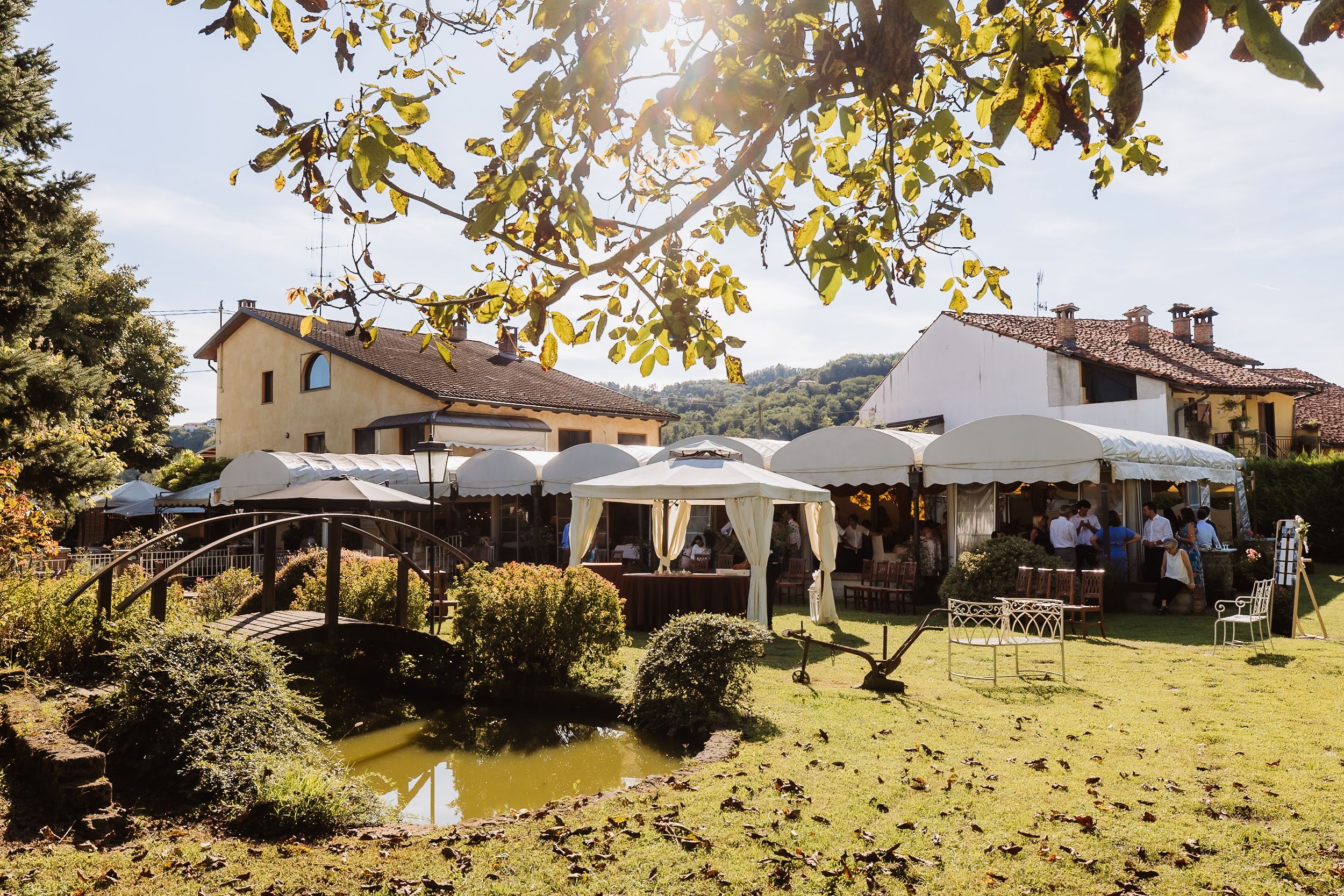 A panoramic view of a rustic outdoor wedding venue with white tents and lush greenery in a countryside setting.