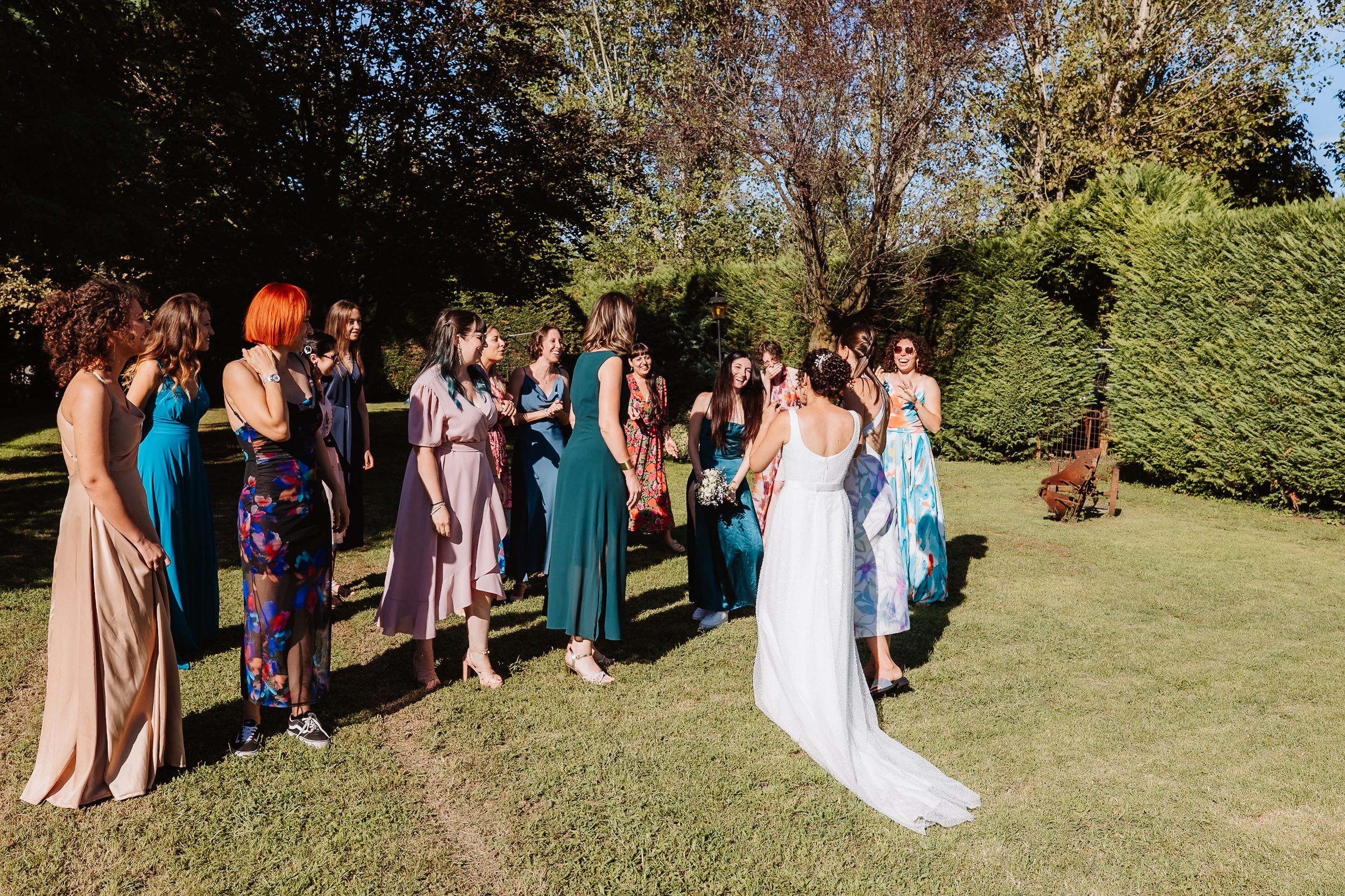 Wedding party poses for group photos in a sunny garden setting with lush green grass and trees in the background.
