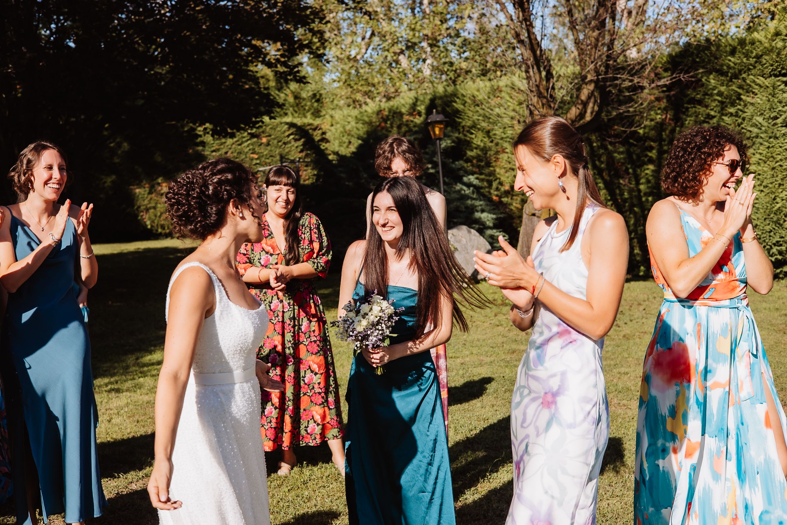 Wedding celebration with bridesmaids in blue dresses gathered on a grassy lawn during an outdoor event.