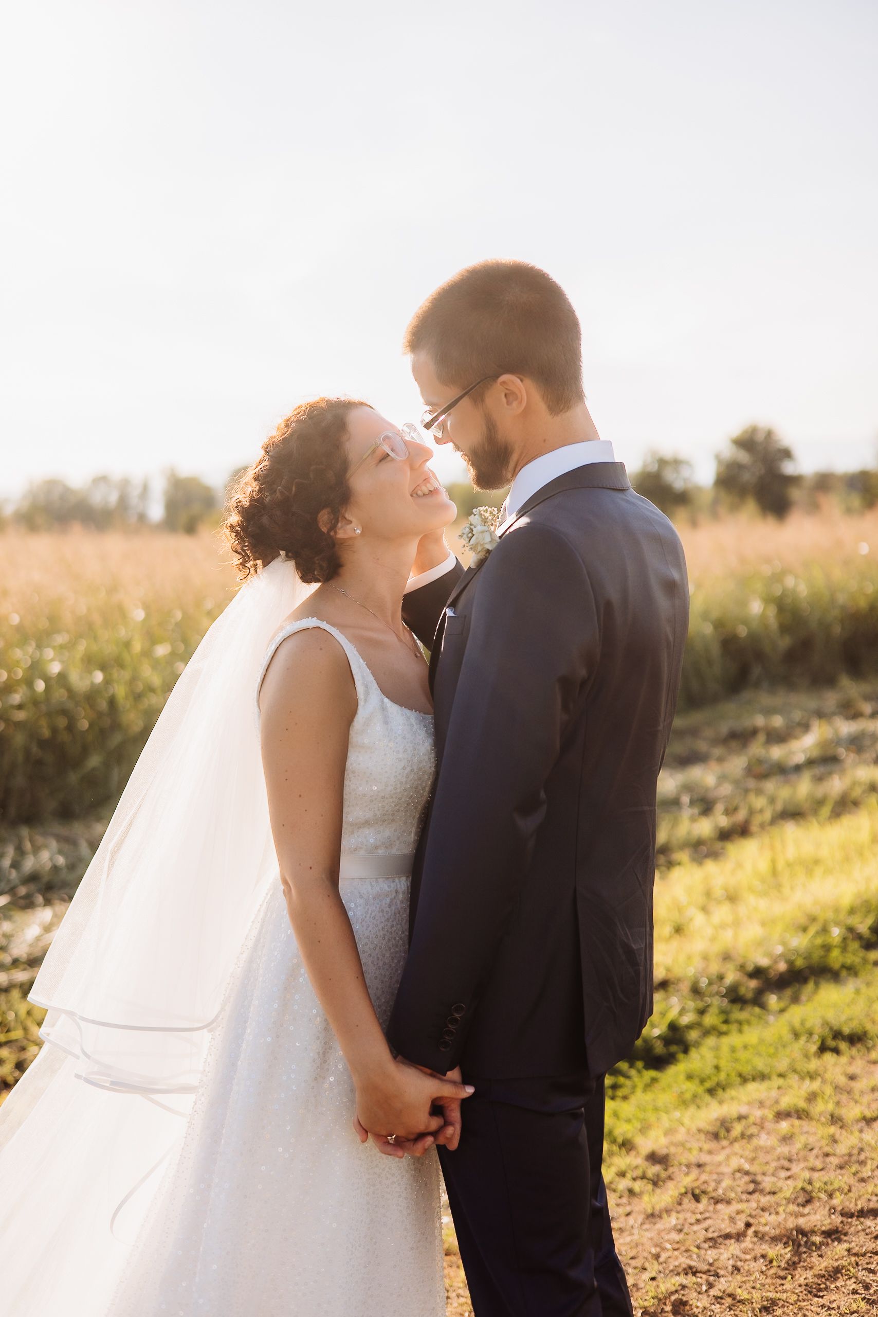 A bride and groom share an intimate moment during their golden hour wedding photo session in a sunlit meadow.
