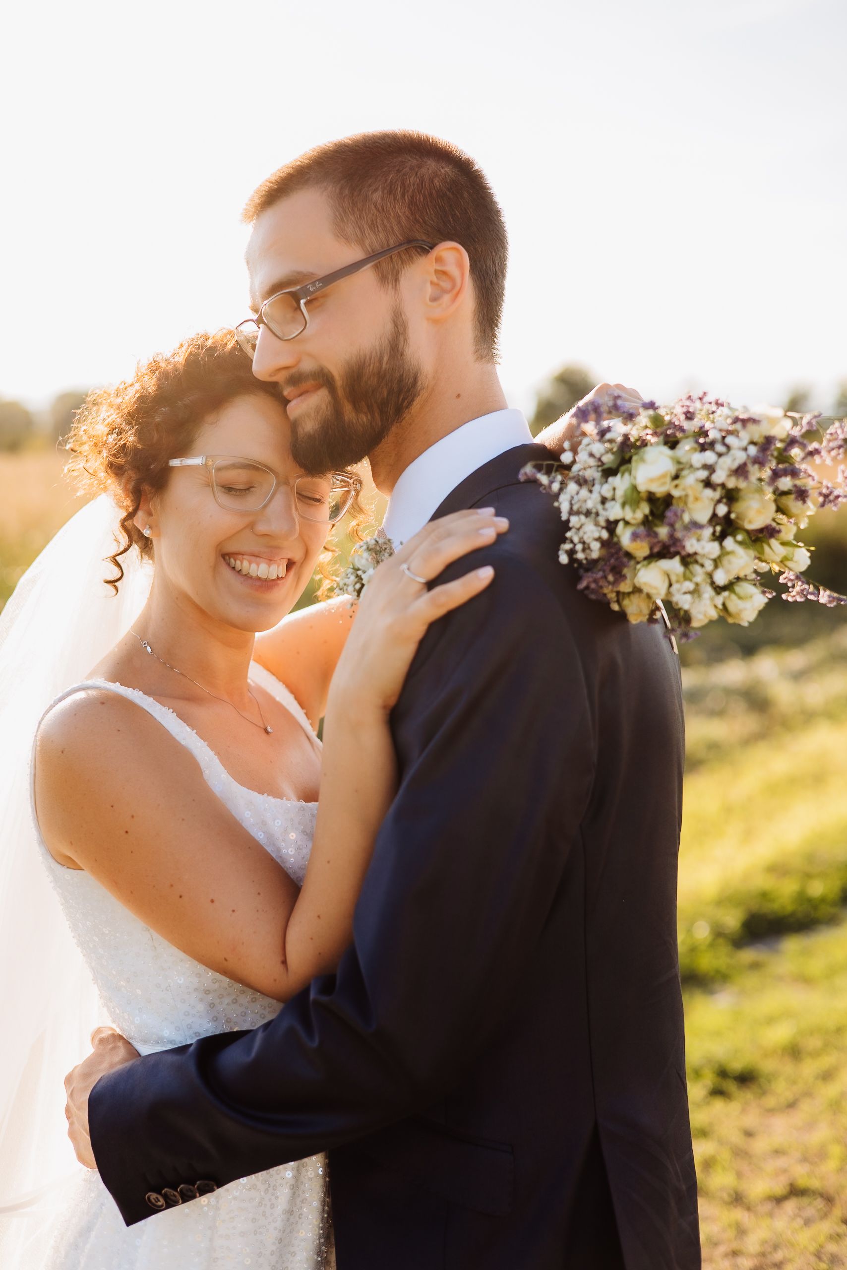 A joyful couple shares an intimate moment during their outdoor wedding ceremony at sunset with a rustic bouquet.