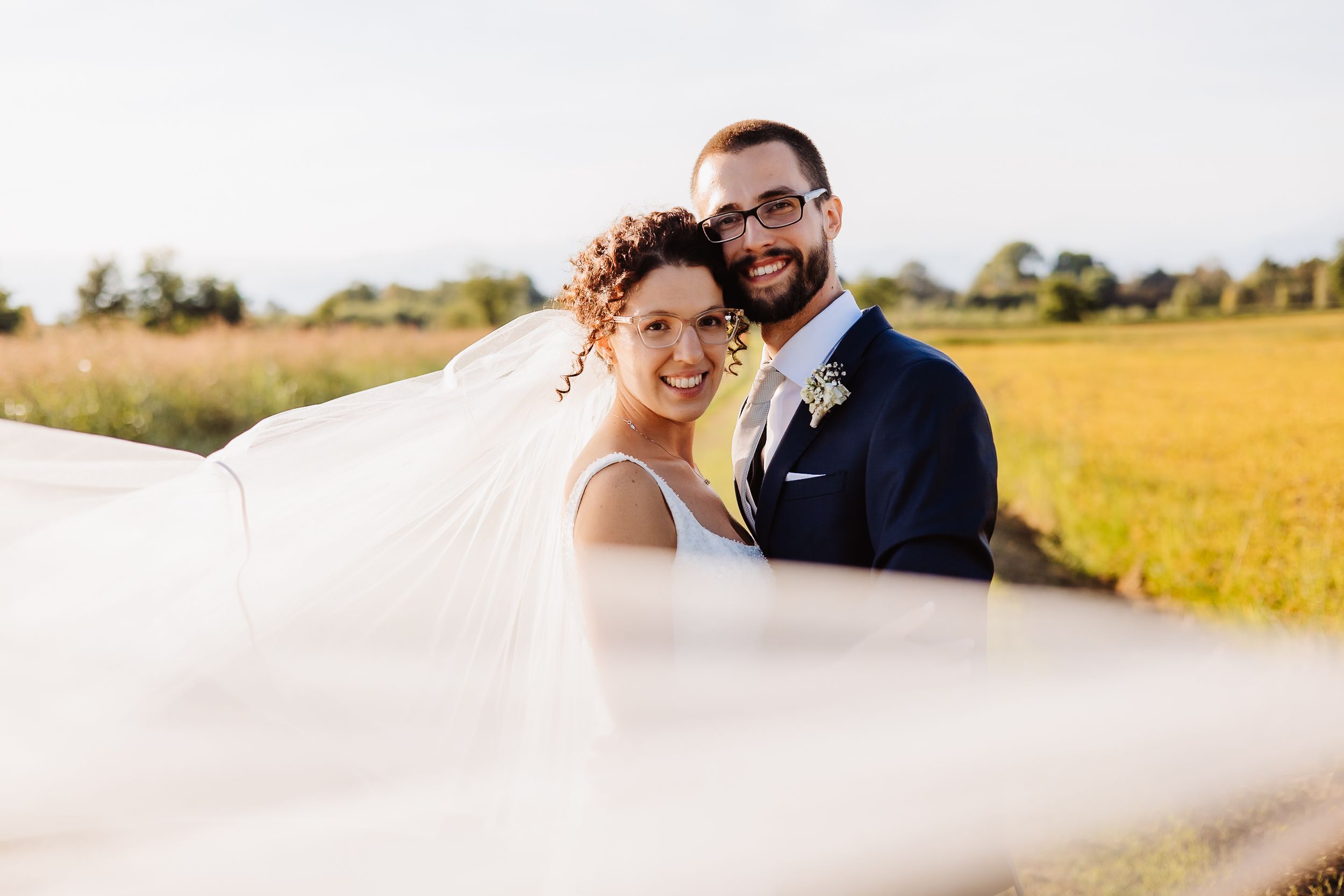 A joyful wedding couple embraces in a golden sunlit field during their outdoor autumn photoshoot.