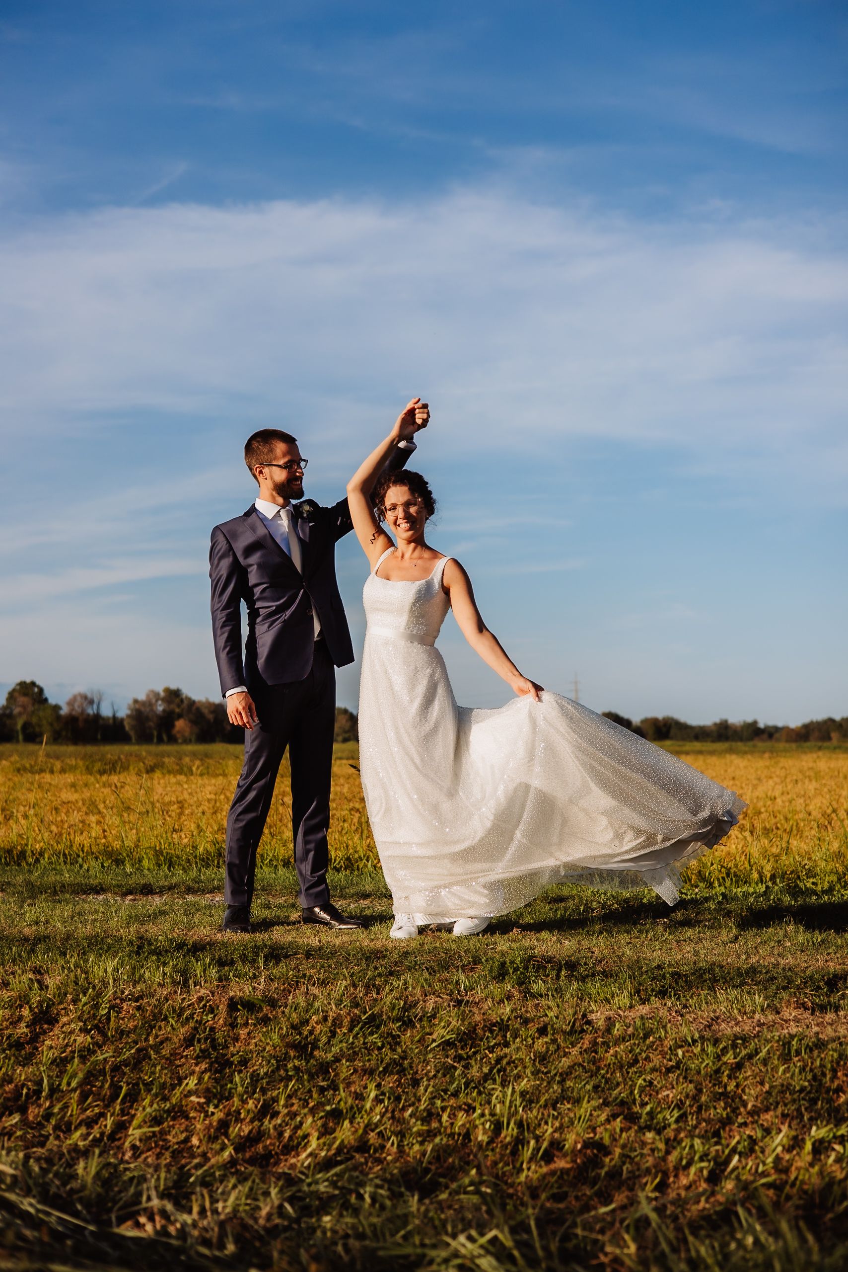 A couple in wedding attire walks through a golden field under blue skies in a series of romantic photos.