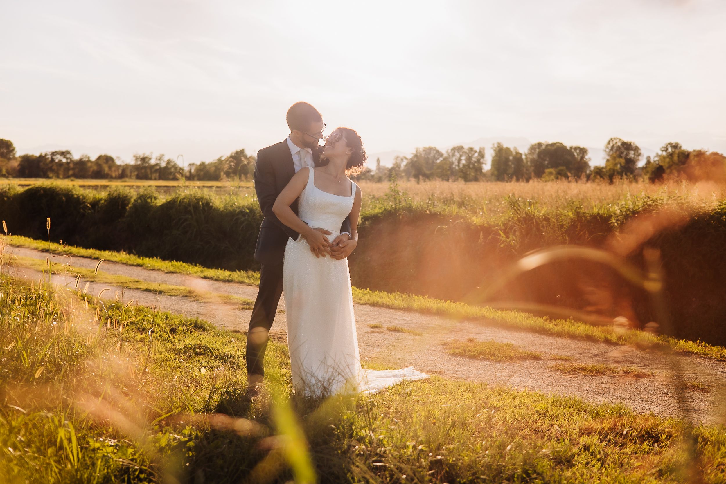 Romantic couple walks along a gravel path at sunset in a golden field.