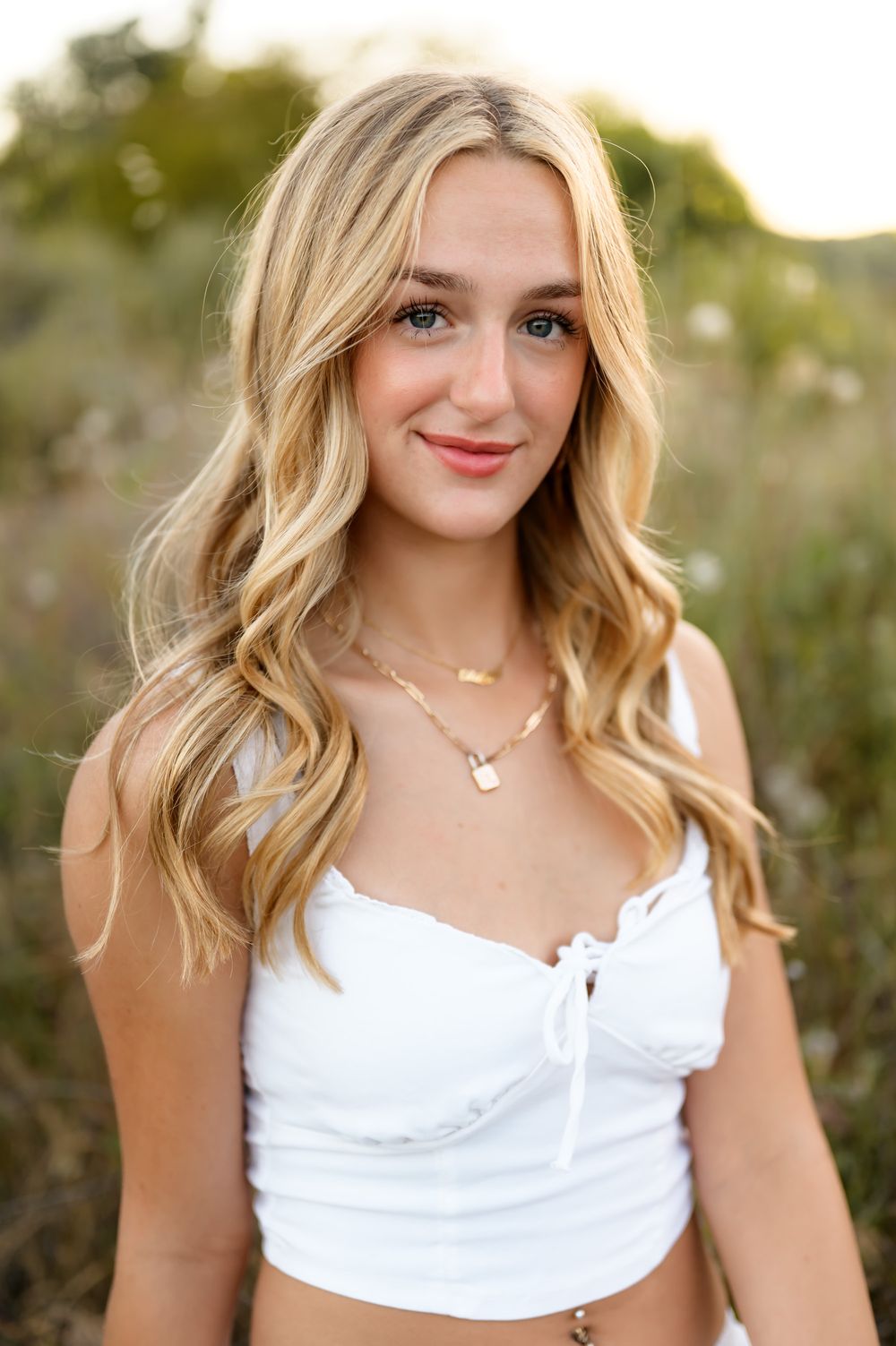 Blonde high school senior wearing white dress sits in wildflowers during outdoor senior portrait session Ventura photographer