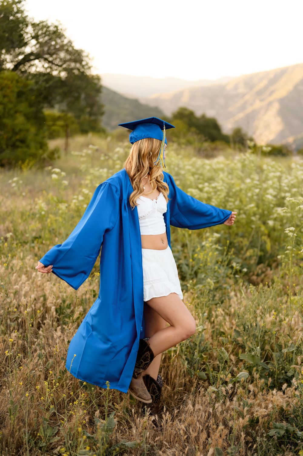 Blonde high school senior wearing white dress dances in wildflowers during outdoor senior portrait session Ventura photographer