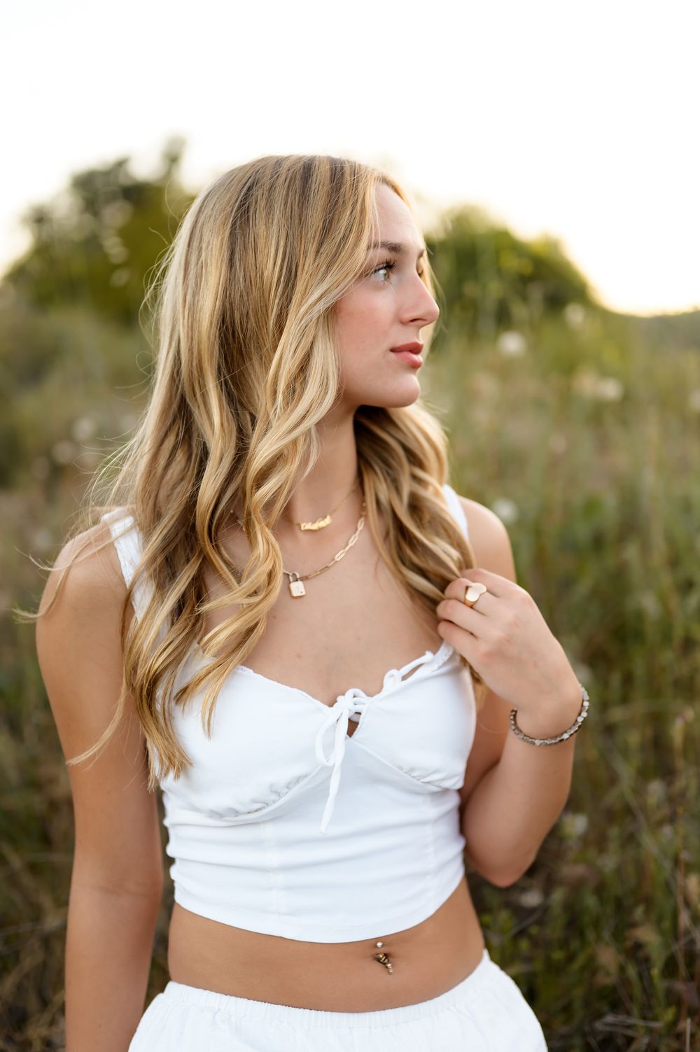 Blonde high school senior wearing white dress sits in wildflowers during outdoor senior portrait session Ventura photographer