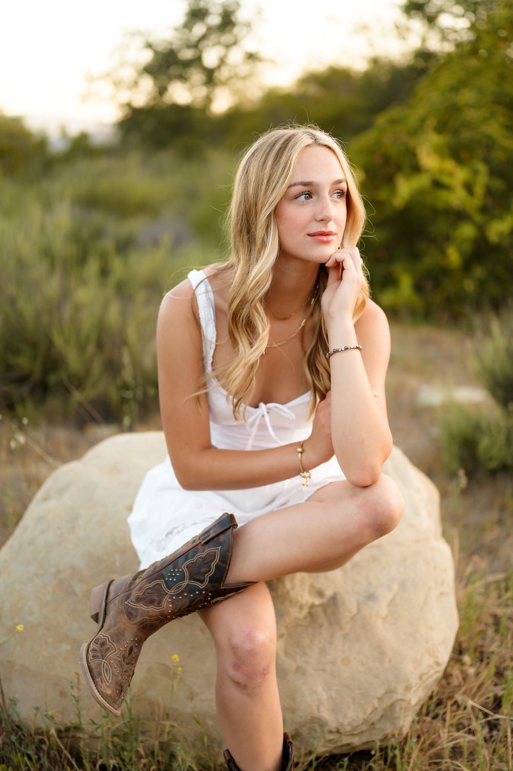 High school senior sits on boulder in white dress & cowboy boots at Ojai Preserve during senior portrait session Ventura photographer