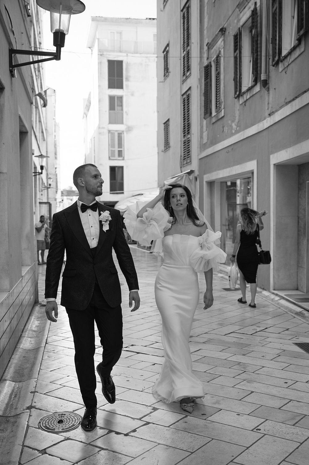 A wedding couple walks down a charming narrow European street in black and white.