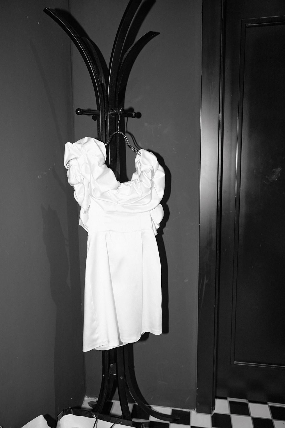 A white dress shirt hangs illuminated against a dark background in a dramatic black and white photograph.