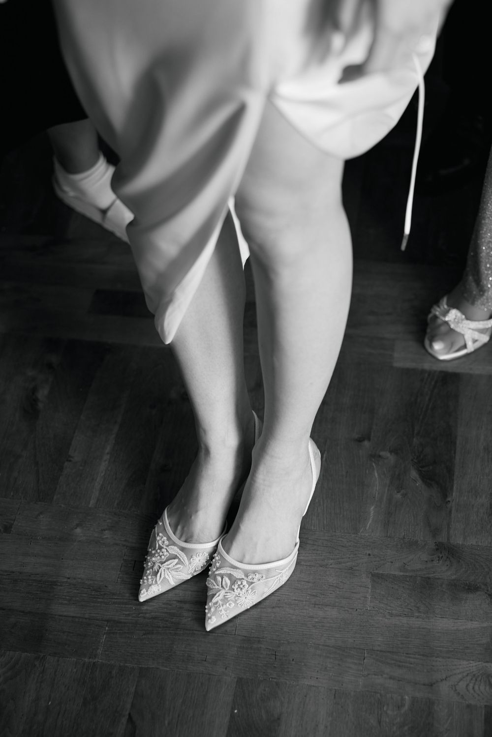 Black and white photo series showing elegant bridal shoes with lace details and pointed toes on a hardwood floor.