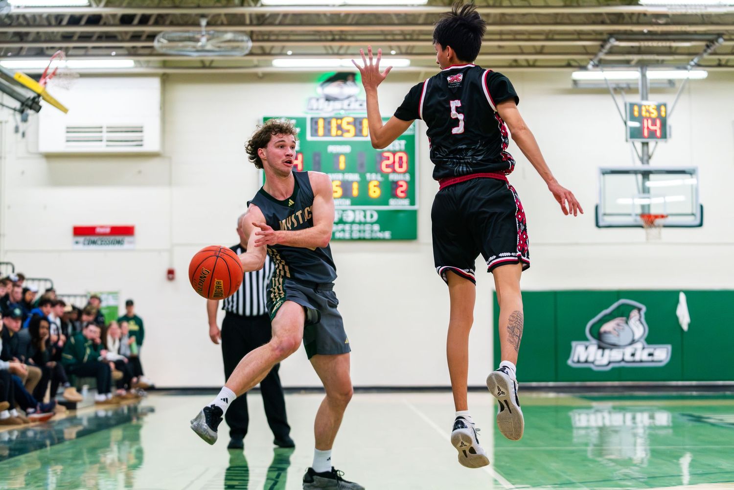 High school basketball players compete during an intense game as one player drives while another leaps to defend.