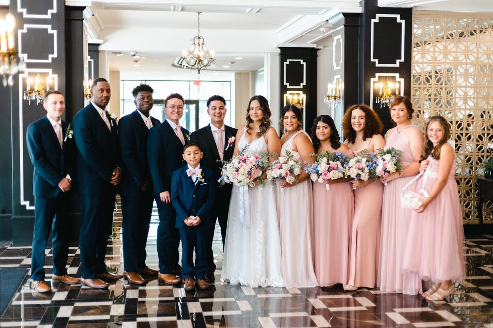 Wedding party poses in navy suits and pink dresses on a black and white checkered floor.