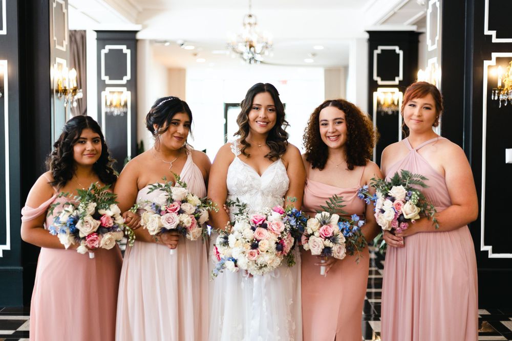 Wedding party in pink bridesmaid dresses and white gown gather together holding matching pastel floral bouquets.