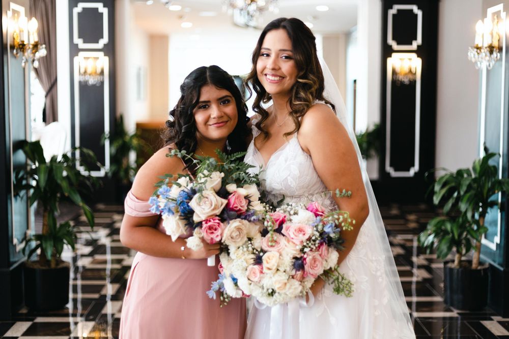 A bride in white stands with her bridesmaid in pink, both holding beautiful floral bouquets.