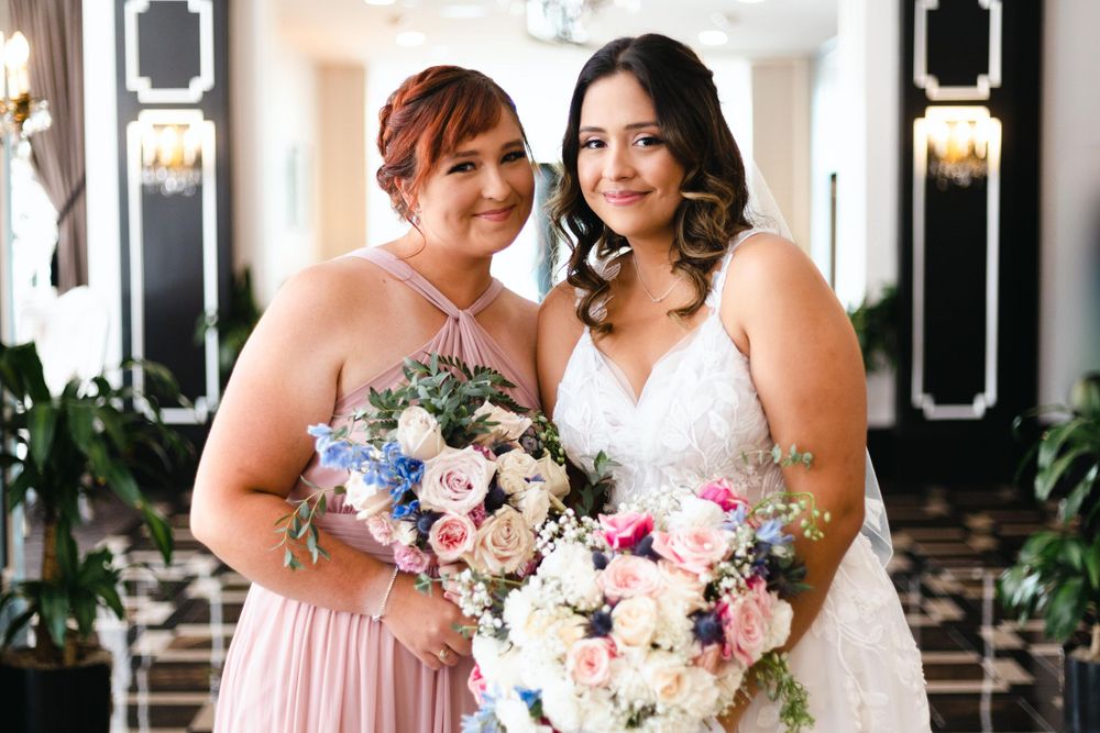 Wedding party members share a joyful moment while holding beautiful pink and white floral bouquets in an elegant venue.