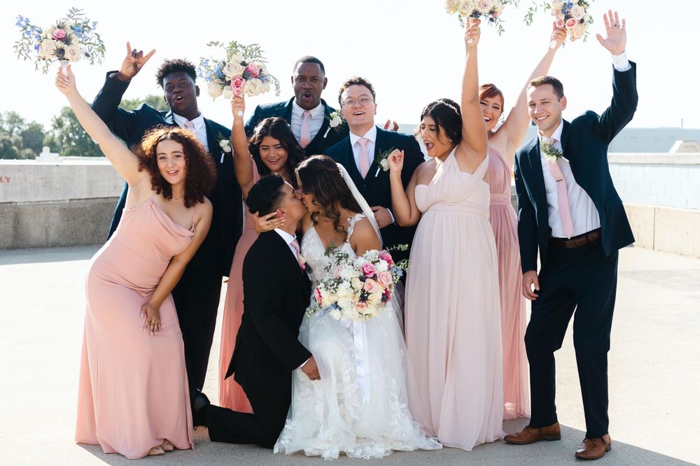 Wedding party celebrates joyfully outdoors with bridesmaids in pink and black dresses.