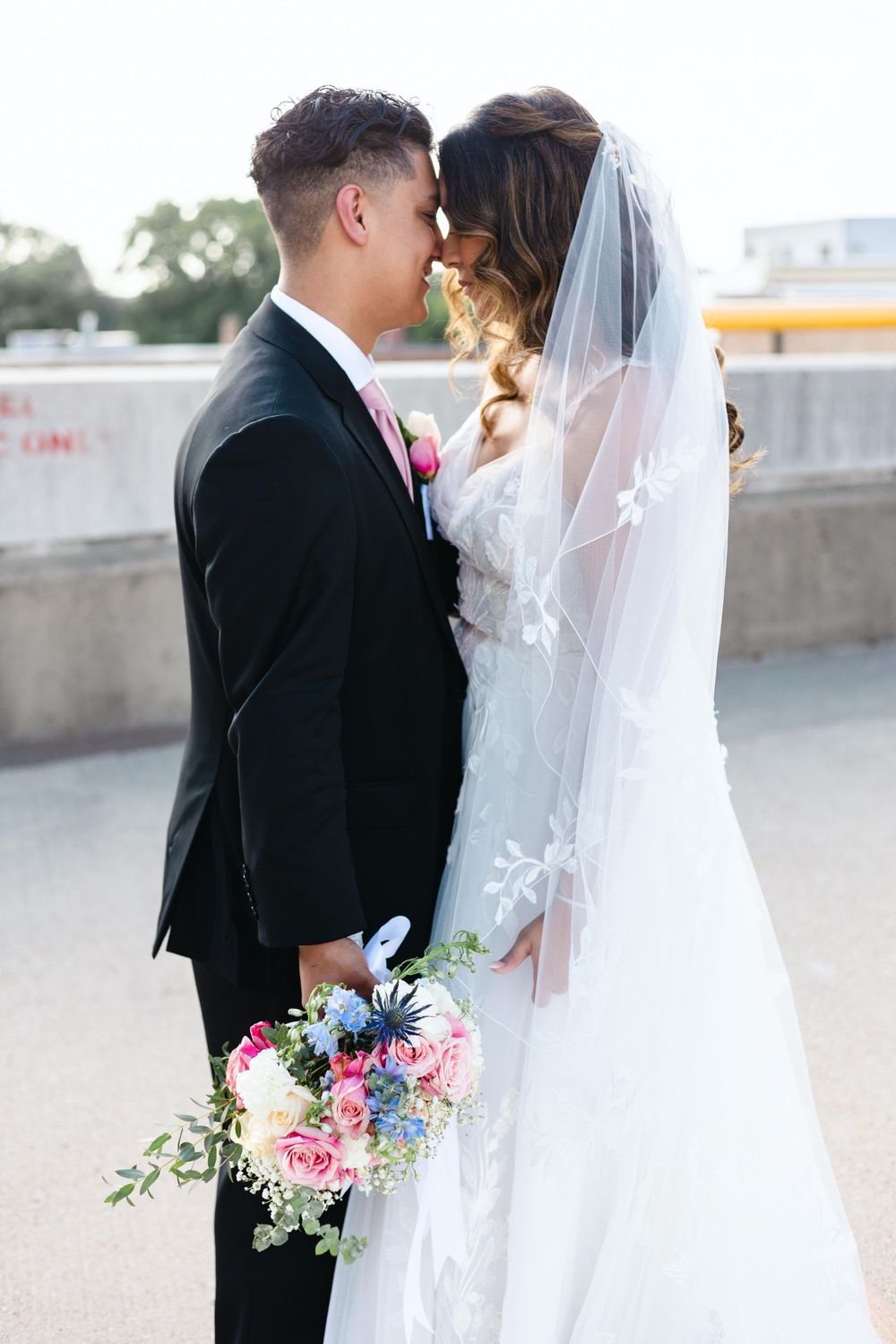 A romantic wedding couple shares an intimate moment while holding a colorful floral bouquet on their special day.
