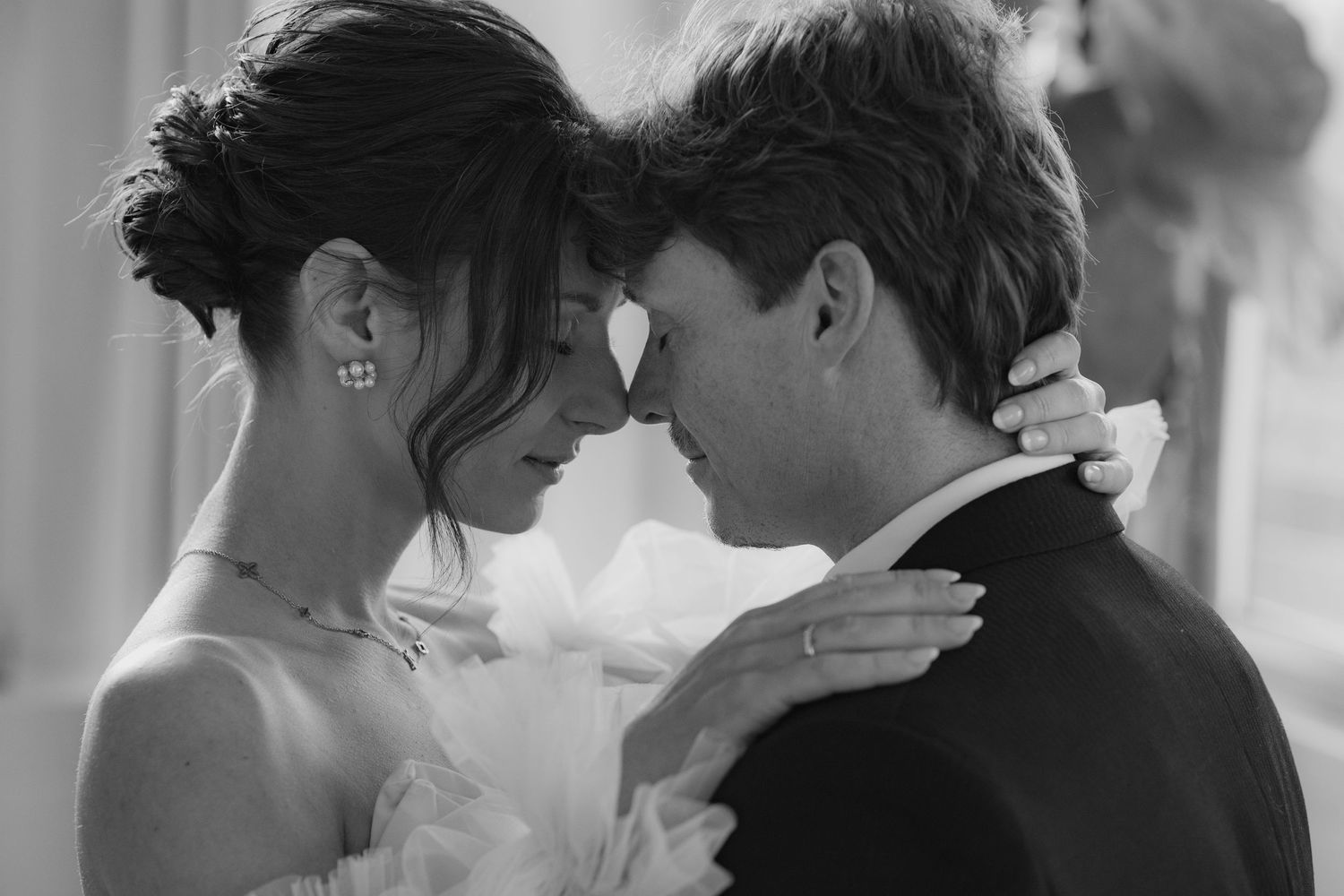 A romantic black and white wedding photo showing a tender moment between newlyweds in formal attire.