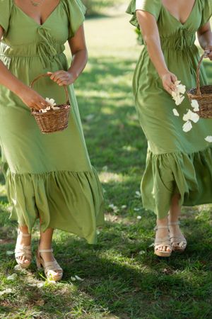 Row of bridesmaids in matching sage green dresses holding flower baskets.