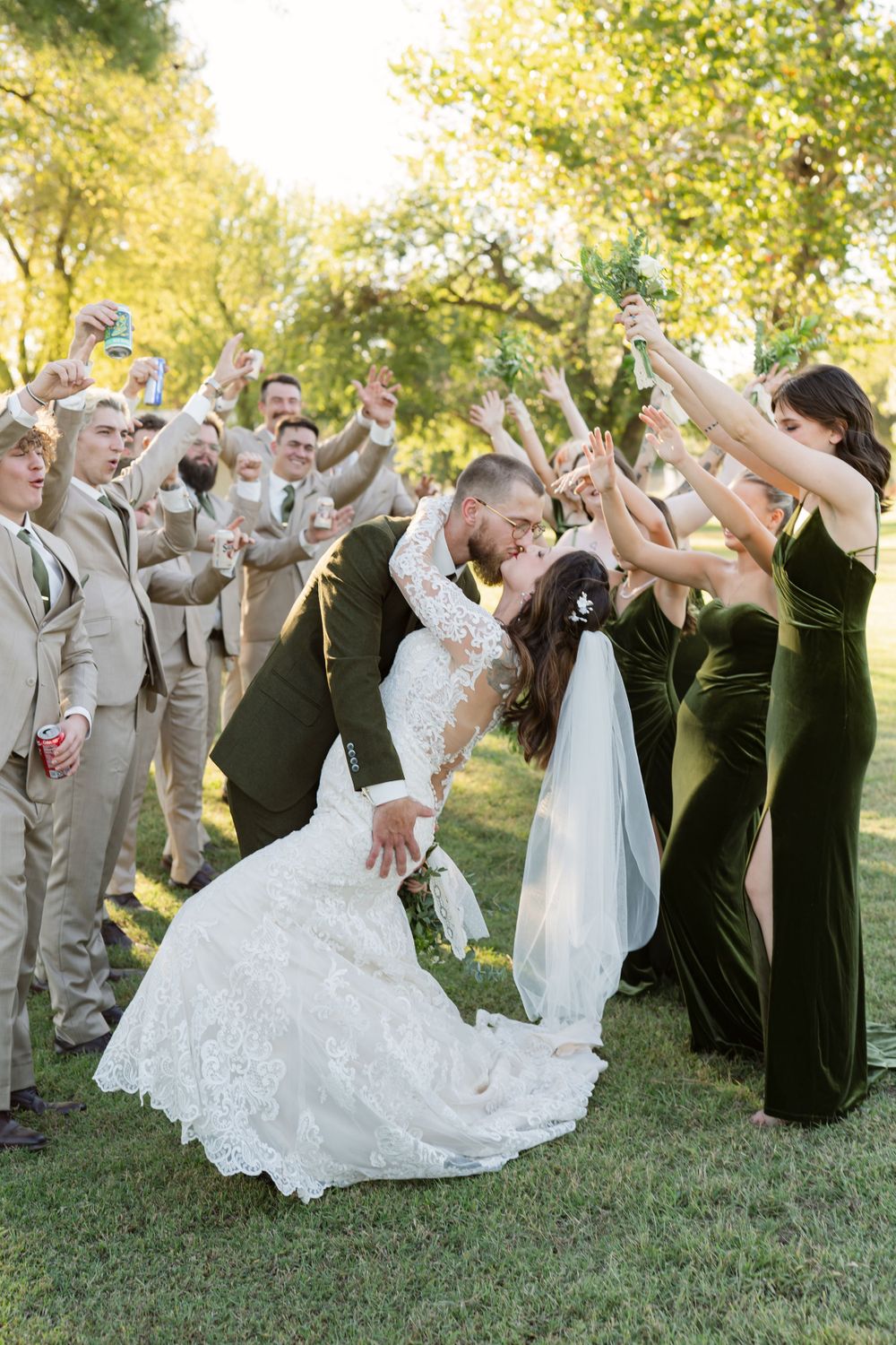 Wedding party members perform choreographed poses on grass during photo session.