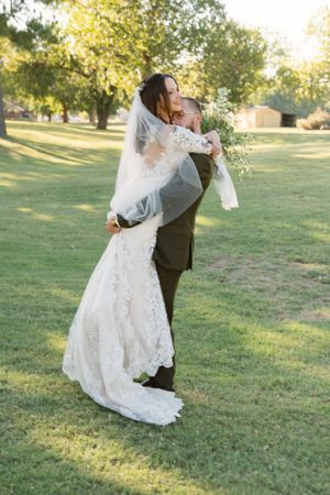 Romantic outdoor wedding dance pose with lace dress on grassy field.