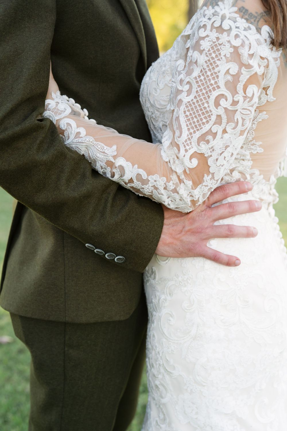 Close-up details of intricate lace sleeves and gentle embrace during wedding portraits.