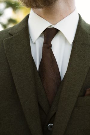 Classic dark suit with brown tie and crisp white collar detail.