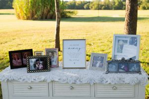 Wedding memorial display with framed photographs arranged on a white tablecloth outdoors.