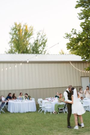 String lights illuminate an outdoor wedding reception setup with white tables and chairs.