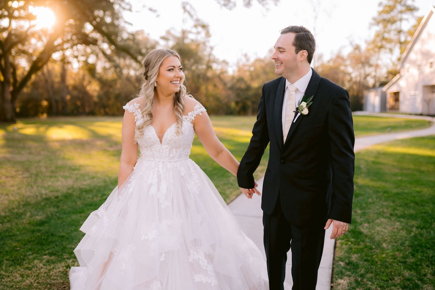 A couple walking hand in hand on their wedding day during golden hour sunset in a grassy field.