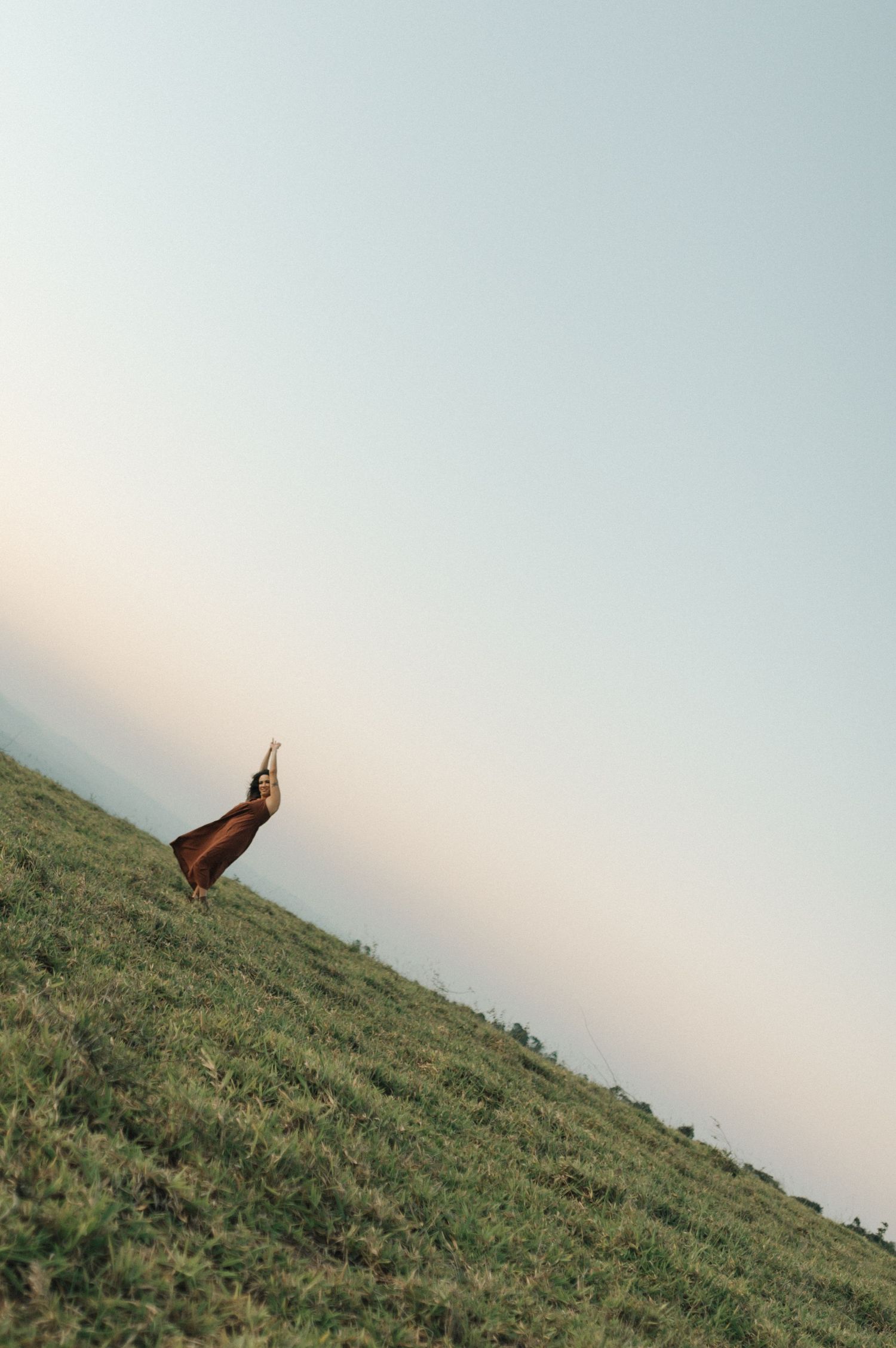 Artistic silhouette of a figure standing on a hillside against a bright sky.