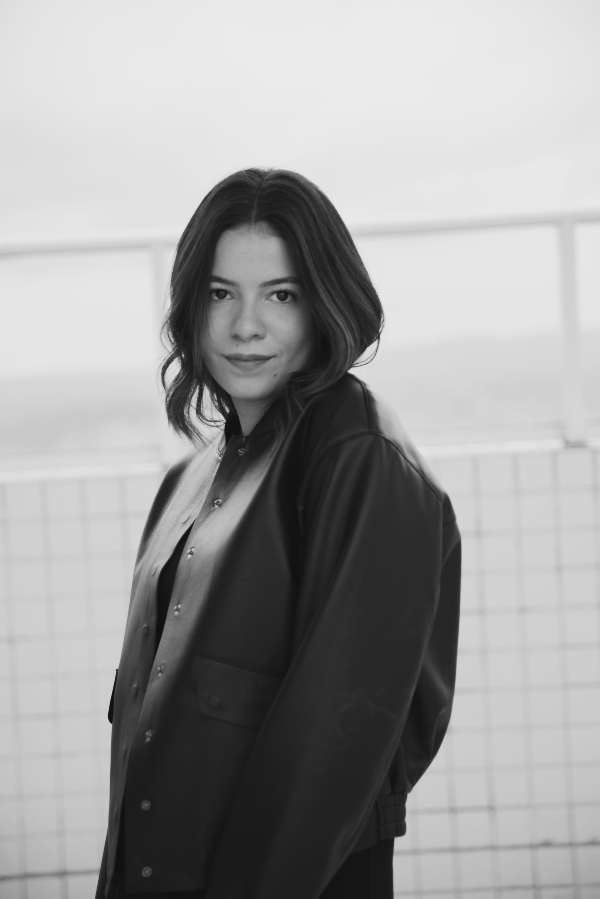 Monochrome portrait in oversized blazer with subtle smile against white background.