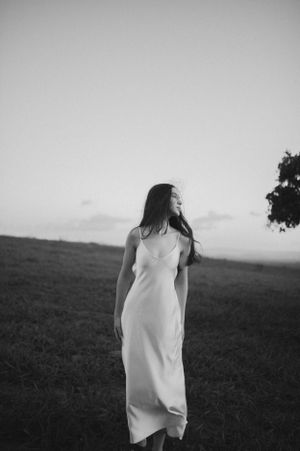 Ethereal black and white portrait of figure in flowing white dress against rural landscape.
