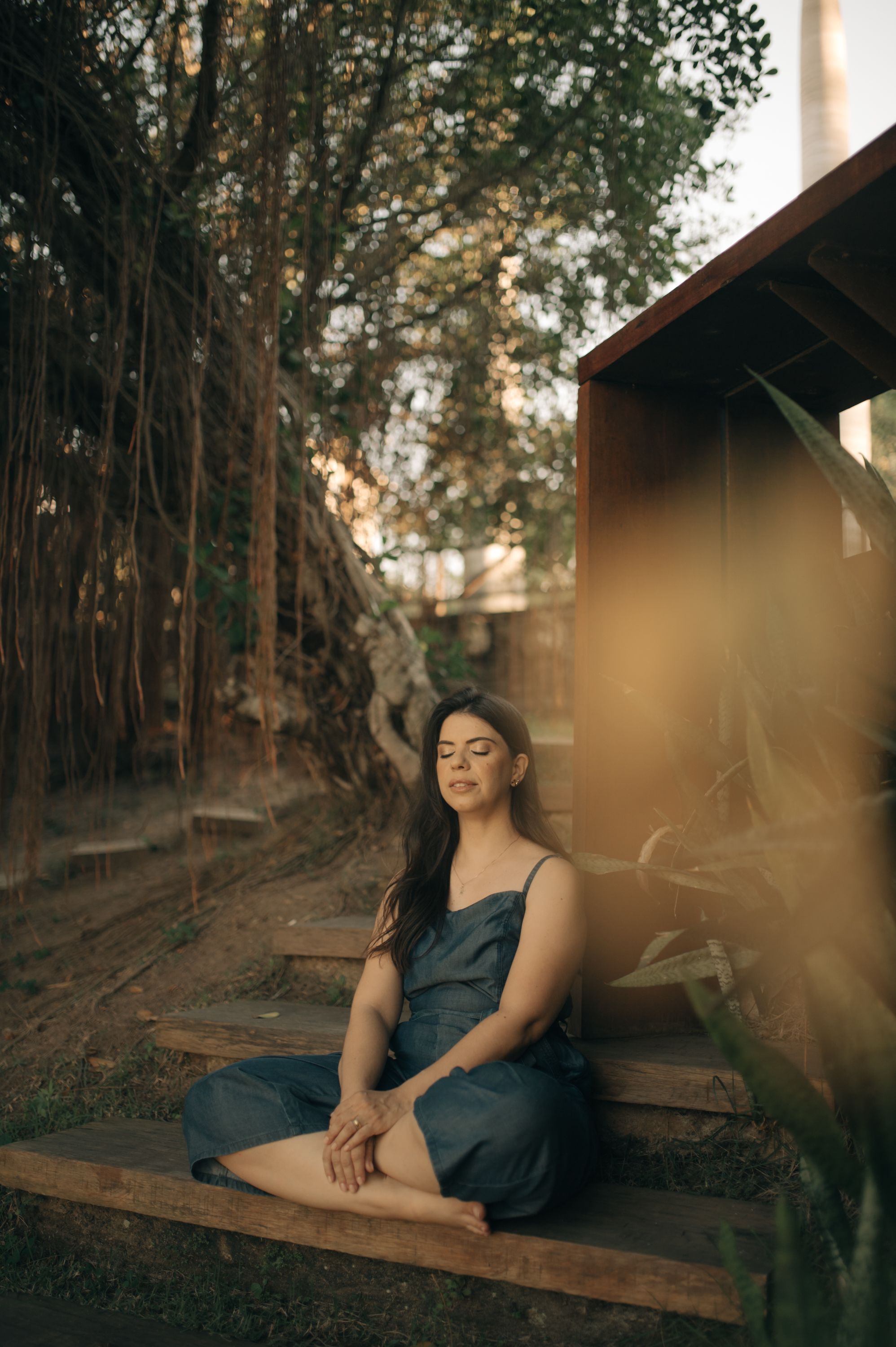 A peaceful outdoor portrait photoshoot featuring a dark blue dress against a rustic wooden backdrop and lush trees.