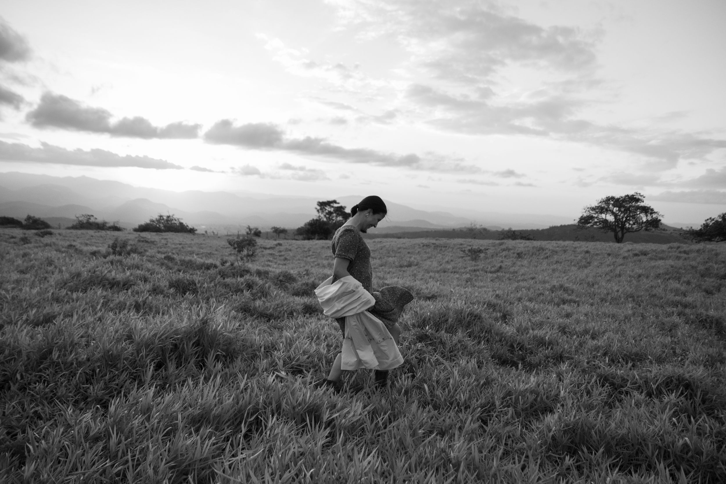 Black and white photo of two people embracing in a grassy field at sunset.