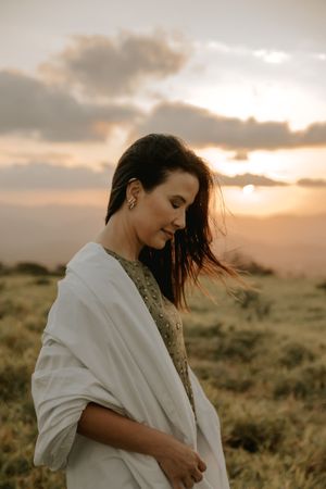 Artistic portrait at golden hour with windswept hair against a sunset sky.