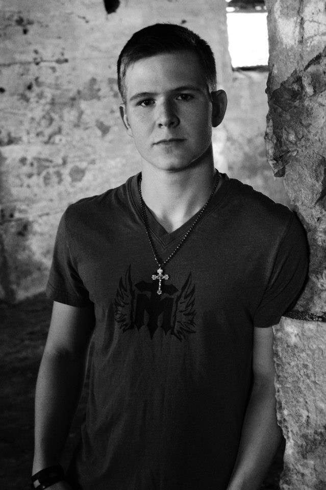 A man in a t-shirt casually leans against a wall, exuding a relaxed and confident demeanor.
