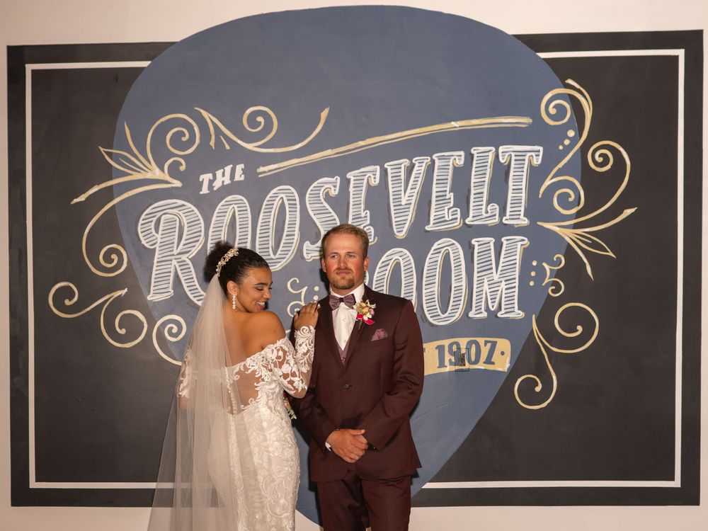 A couple poses in formal attire in front of a vintage Roosevelt Room sign.