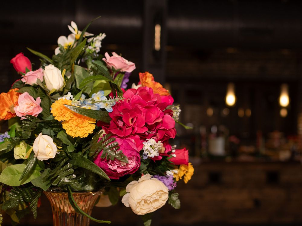A vibrant floral arrangement with pink, orange and white flowers in a vase sits against a dark, dimly lit interior background.