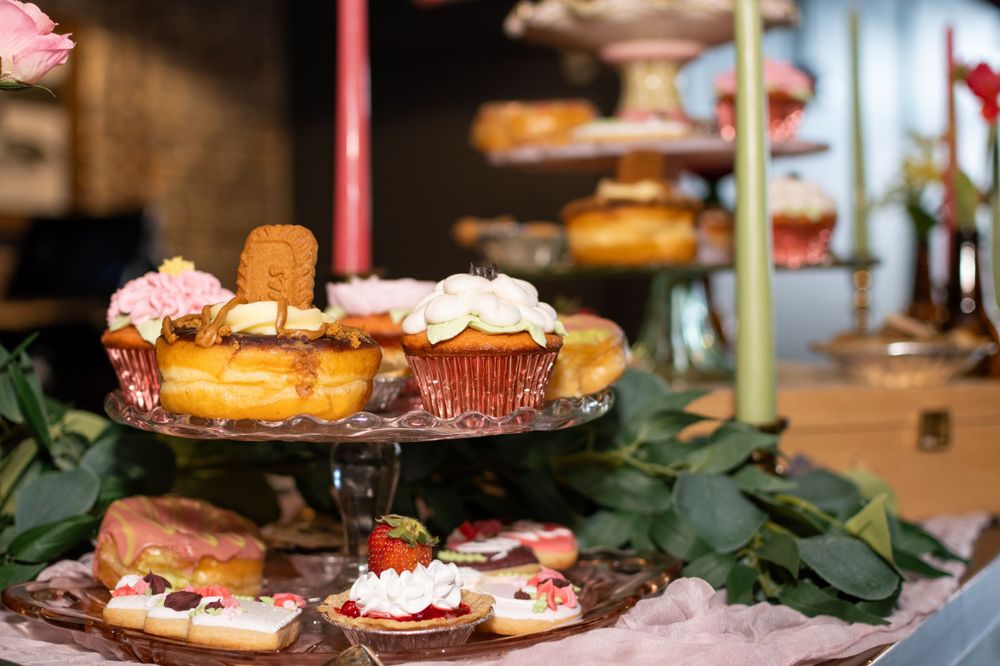 A dessert display featuring cupcakes and pastries with pink frosting on tiered stands among green foliage.