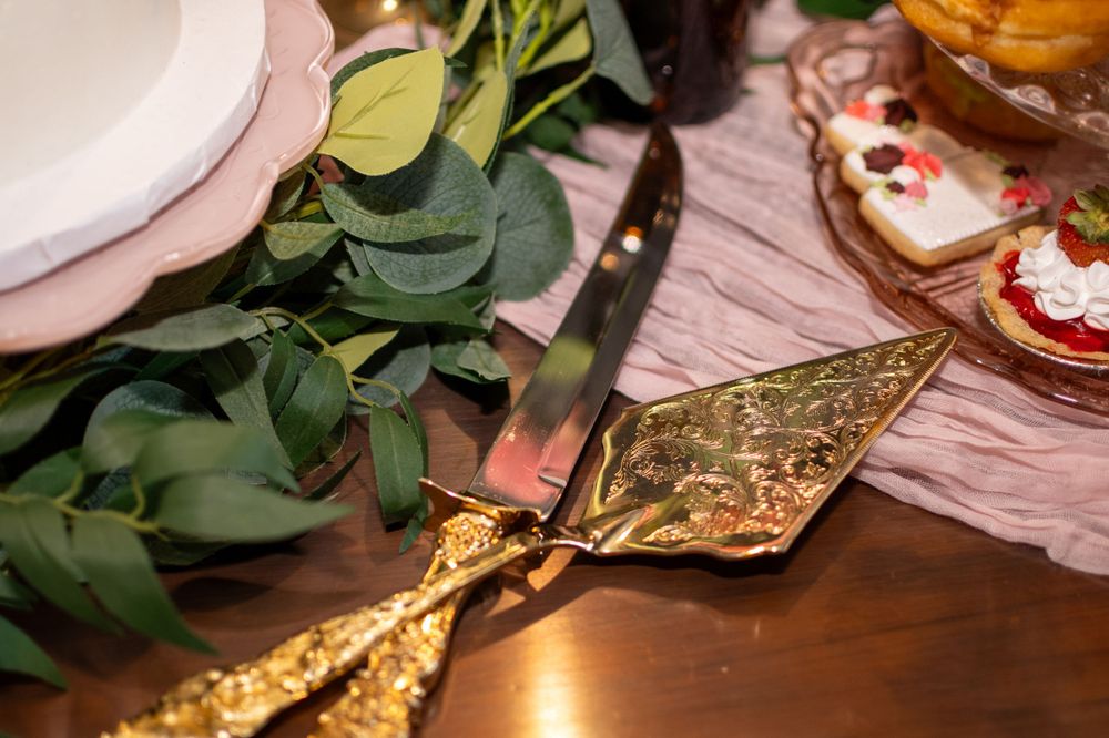 Ornate gold serving utensil rests on wooden table beside green foliage and pink table decor.