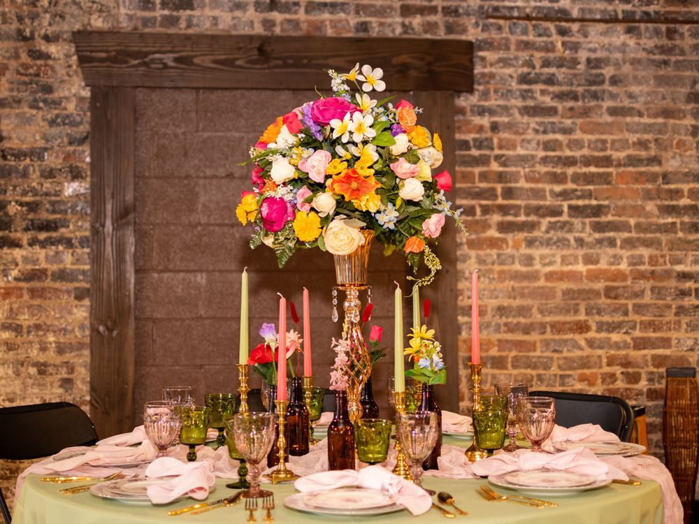 Elegant wedding reception table with tall floral centerpiece, candles and place settings against rustic brick wall.