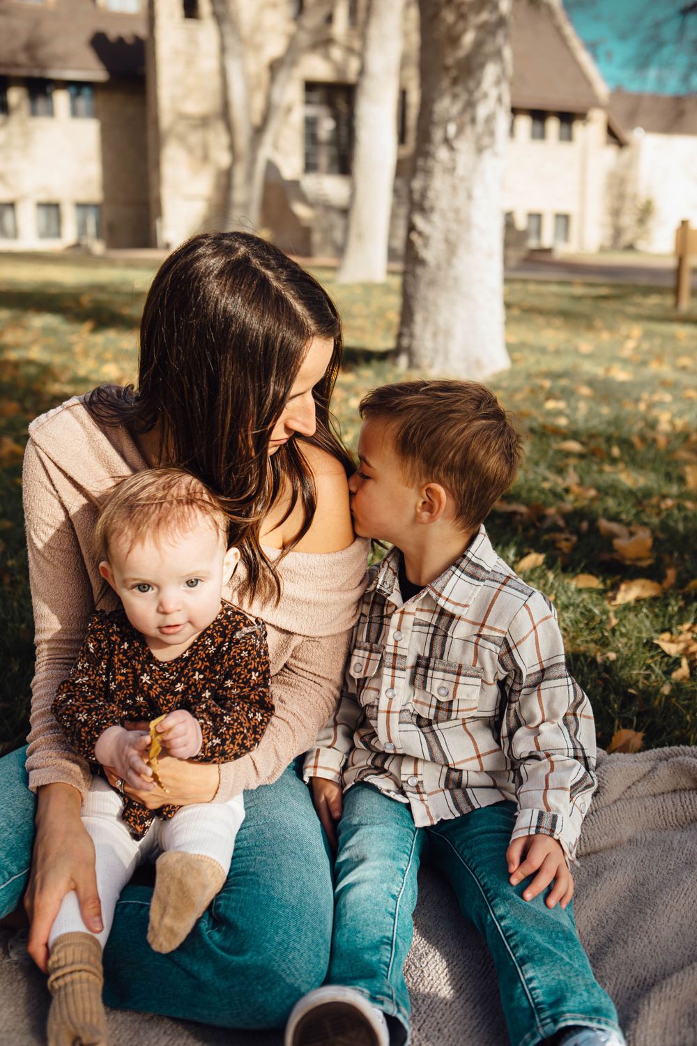 A candid outdoor family moment on blanket in autumn with children as sunlight filters through trees in background.