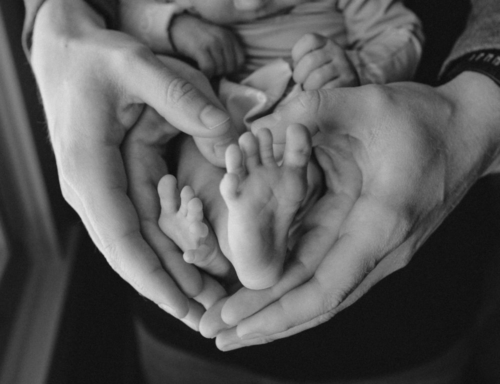 A black and white close-up photo showing tiny baby feet cradled gently in adult hands.