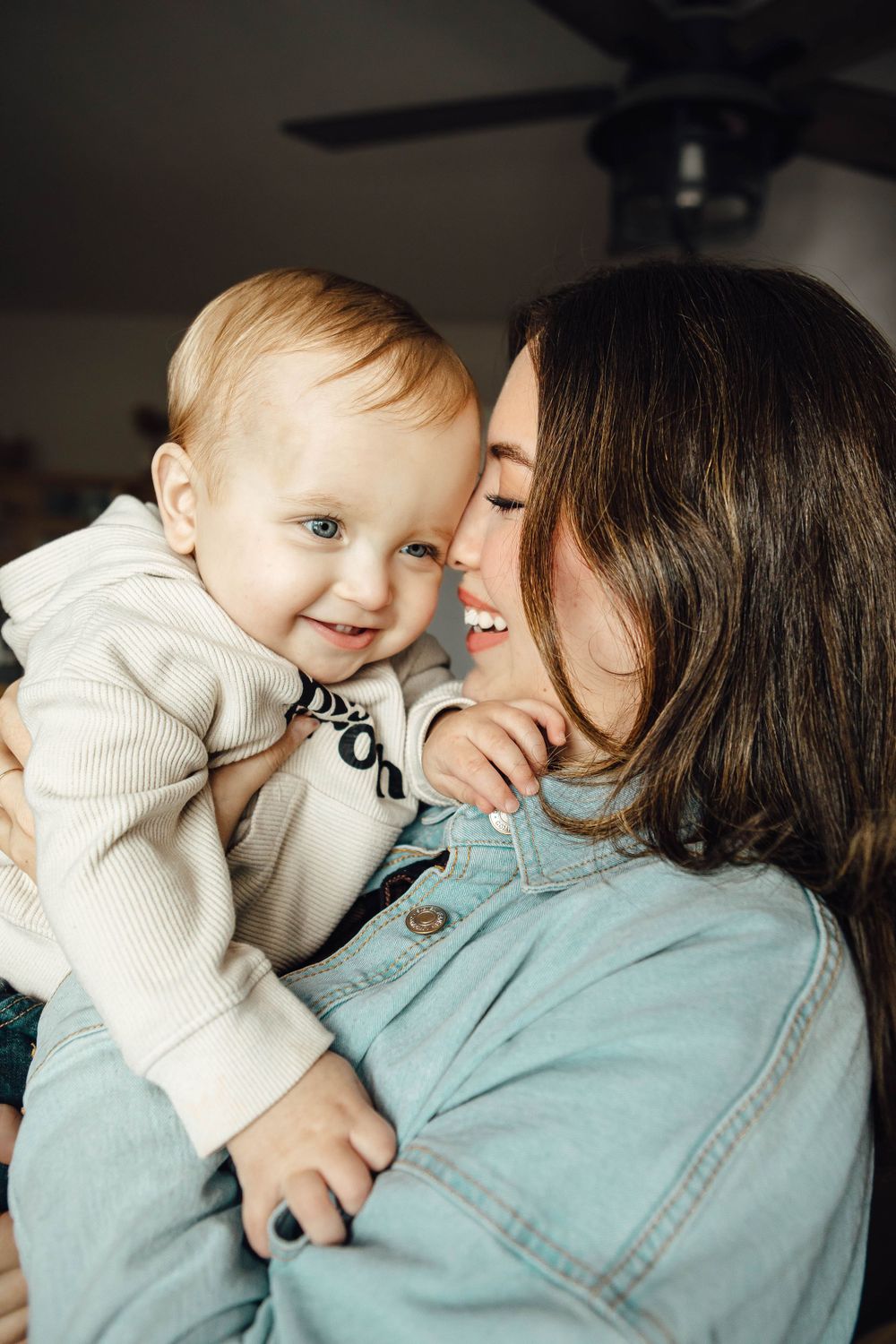 A heartwarming indoor portrait shows a tender moment between parent and baby sharing smiles and affection in natural light.