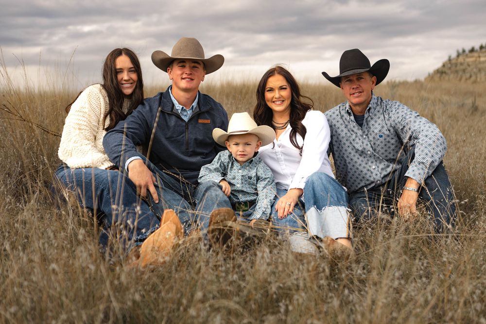 A group in western attire poses casually together on a grassy hillside during an outdoor photo session.