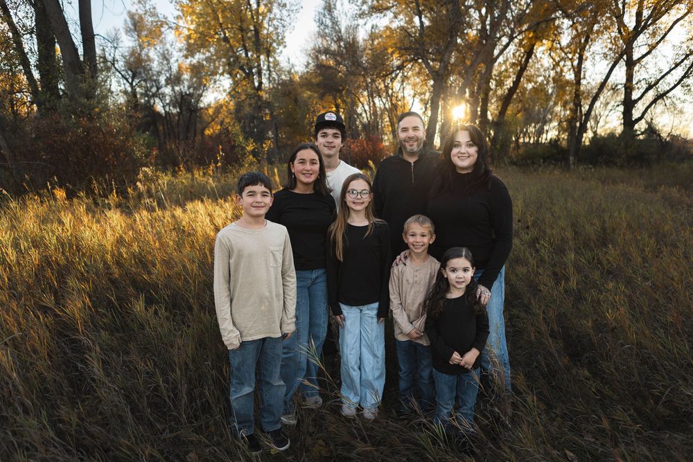 A group stands together in a grassy field at sunset with golden light filtering through autumn trees behind them.