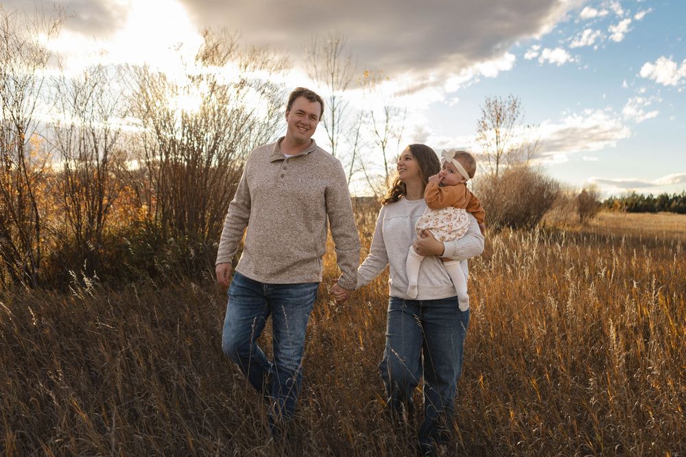 A couple walks hand in hand through a golden autumn field at sunset as warm light illuminates the tall grass.
