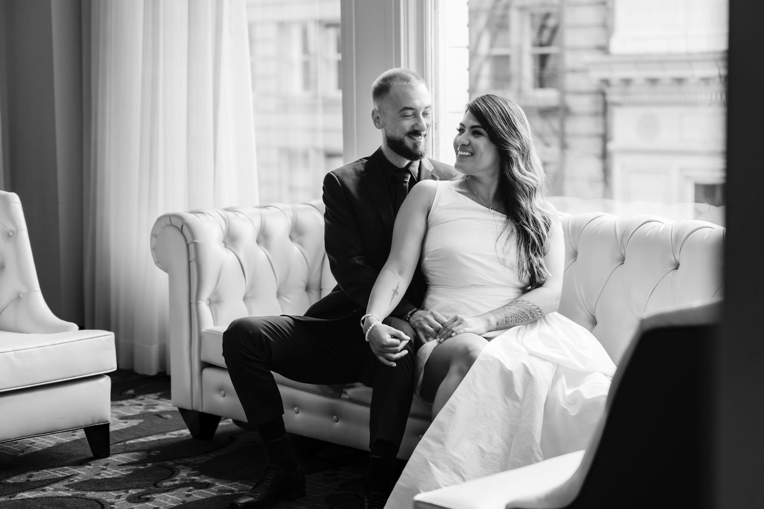 A relaxed black and white portrait of newlyweds seated on an elegant tufted sofa.